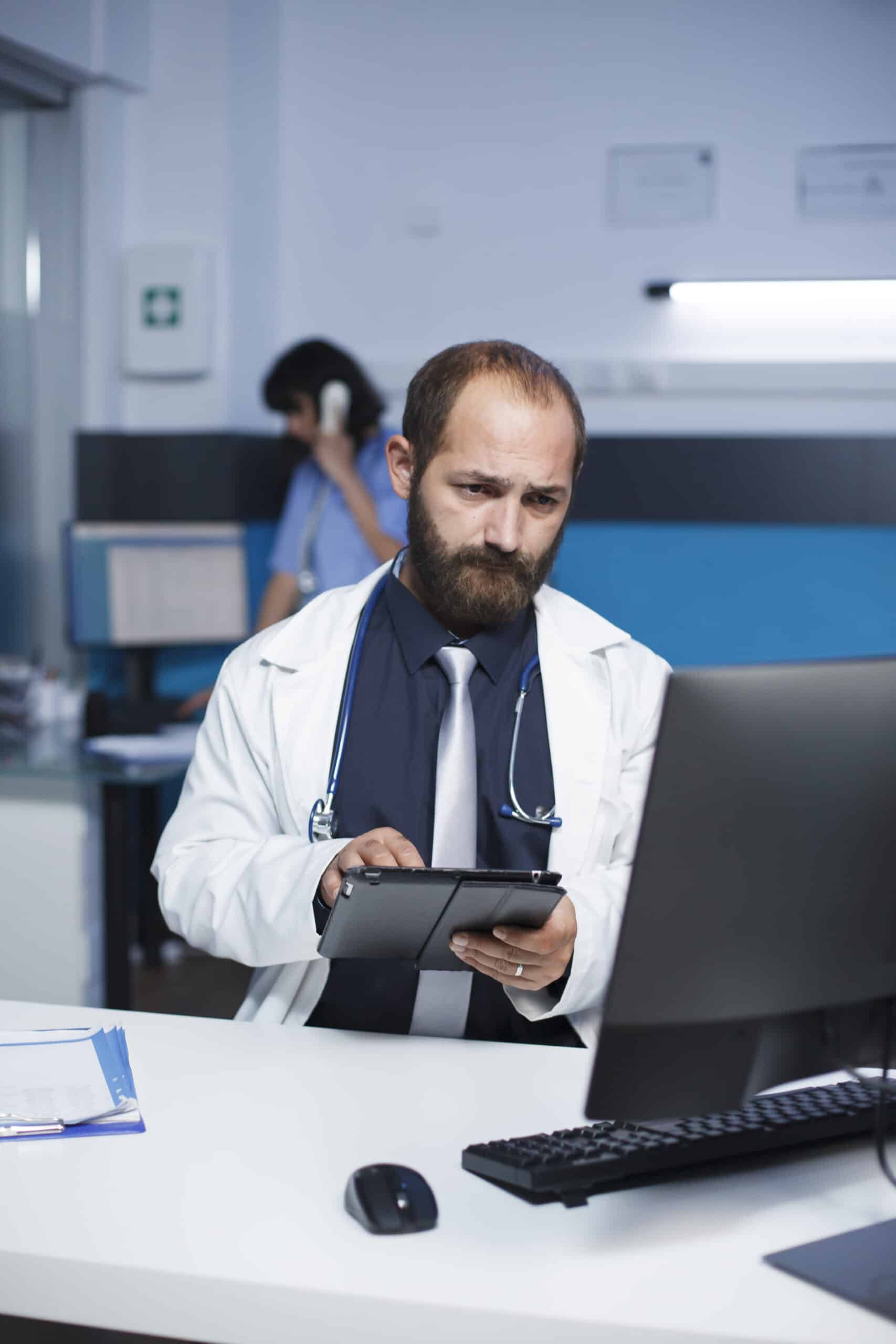 Profesional revisando información en una tablet frente a un computador